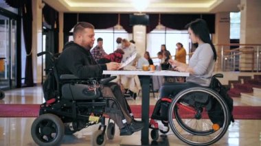 Tekerlekli. Maluliyet. Engelli genç adam ve kadın boyalarla resim çiziyor, masadaki tekerlekli sandalyelerde oturuyorlar. Engelliler için yaratıcı grup dersleri. Eğitim, ilişki ve insanlık