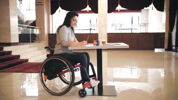 Tekerlekli. Maluliyet. Engelli genç kadın çizim yapıyor, masada tekerlekli sandalyede oturuyor. Engelliler için yaratıcı dersler. Eğitim, ilişki ve insanlık kavramı — Stok video