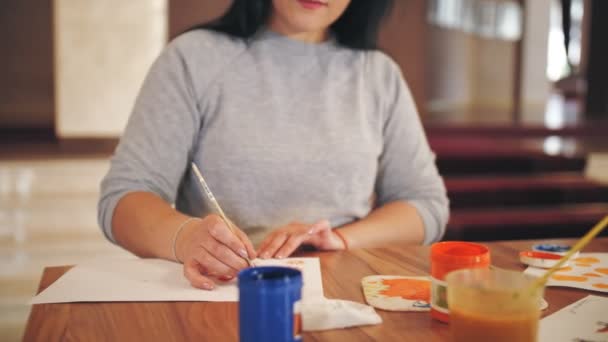 Tekening verf. close-up, portret. Jonge vrouw tekent verf, zit aan tafel. Ze kijkt naar de camera en glimlacht. creatieve lessen. Onderwijs, relatie en menselijkheid — Stockvideo