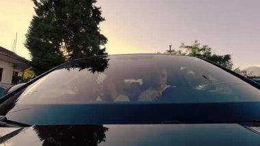Gün batımında seyahat eden aile turistlerinin arabasının ön camından bakın. İçinde neşeli yolcular olan dinamik yolculuk görüntüleri..