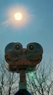 Alp platformuna yerleştirilmiş yeşil dürbünler parlak güneşin altında ve arka planda çıplak ağaçlarla birlikte..