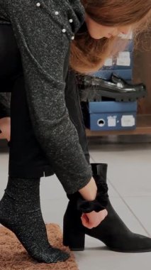 Gri taytlı kadın ayakkabı mağazasında siyah çizme deniyor. Ayakkabı uydurma ve müşteri seçme süreci.