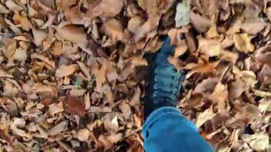 Bir insanın altın sonbahar parkında, şık kış botlarının altında yapraklarla yürüdüğü yakın plan perspektif..
