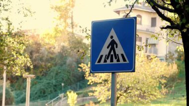 Arka planda bulanık bir sonbahar kasabası manzarası olan yaya geçidi tabelasının yakın çekimi. Yol güvenliğini sağlıyorum..