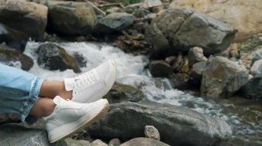 Ormandaki temiz dağ deresinin yanında dinlenen gezgin bacakları görülüyor. Barış ve doğa ile birliğin atmosferi.