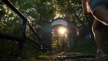 Yaşlı bir taş kemerin yakınındaki ormanda yürüyen dişi turist. Gizemli bir orman çalılığında taşlardan yansıyan güneş ışınları..