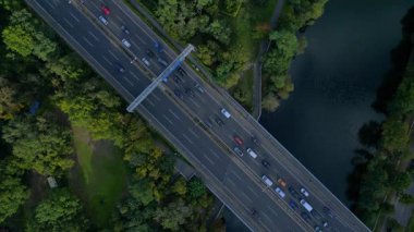 Hava görüntüsü, ağaçlarla çevrili bir nehrin üzerinden geçen yoğun bir karayolu trafiğini gösteriyor. dikey kuş bakışı dron 