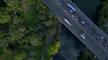 Hava görüntüsü, ağaçlarla çevrili bir nehrin üzerinden geçen yoğun bir karayolu trafiğini gösteriyor. dikey kuşların göz teması uçuş üstü insansız hava aracı 