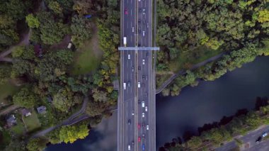 Hava görüntüsü, ağaçlarla çevrili bir nehrin üzerinden geçen yoğun bir karayolu trafiğini gösteriyor. İHA kamerası aşağıya bakıyor 
