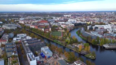 Berlin 'de sonbaharda bir nehir, şehir binaları ve bir futbol sahası bulunur. geniş yörünge görünümü dronu 