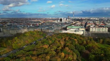 Berlin 'in tarihi Brandenburg Kapısı manzarası, şehir binaları, sonbaharda yeşil Tiergarten parkı. Hız rampası hiper hareket zamanı hızlandırılmış panorama yörünge dronu 