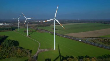 Rüzgâr tarlası türbinleri işlek bir otoyolun yanındaki yeşil alanlarda temiz elektrik üretiyor. panorama genel görünüm dronu 