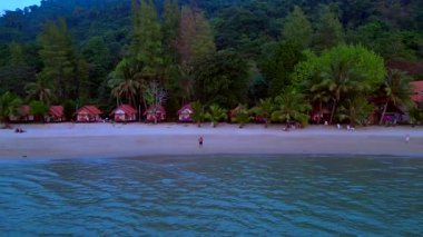 Koh Chang 'deki palmiye ağaçlarının altında insanların kumsalda ve bungalovlarda yürüdüğü tropik bir sahil tıpkı Tayland' daki eski güzel günlerdeki gibi. doly sağ drone 