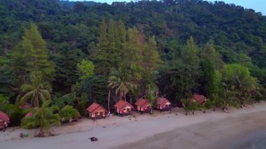 Koh Chang 'deki palmiye ağaçlarının altında insanların kumsalda ve bungalovlarda yürüdüğü tropik bir sahil tıpkı Tayland' daki eski güzel günlerdeki gibi. uçuş üstü insansız hava aracı 