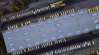 Yükleme rıhtımlarına park etmiş çok sayıda kamyonu olan büyük bir depo tesisi, küresel dağıtımı temsil ediyor. dikey kuşların bakış açısı sağdaki drona döndür 