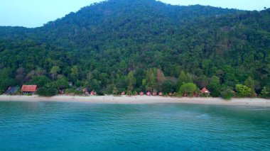 Kıyı boyunca bungalovları olan Koh Chang Tropikal plajı ve bir dağı kaplayan yoğun yeşil orman. panorama genel görünüm dronu 