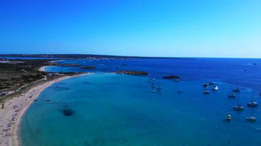 Platja de ses Illetes 'in açık turkuaz okyanuslu plaj formenterasını ve açık bir gökyüzü altında dinlenen insanları gösteren hava manzarası. panorama genel görünüm dronu 