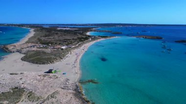 Platja de ses Illetes 'in açık turkuaz okyanuslu plaj formenterasını ve açık bir gökyüzü altında dinlenen insanları gösteren hava manzarası. panorama genel görünüm dronu 