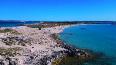 Platja de ses Illetes 'in açık turkuaz okyanuslu plaj formenterasını ve açık bir gökyüzü altında dinlenen insanları gösteren hava manzarası. Uçarken üstten uçmak İHA 'yı ileri itmek 