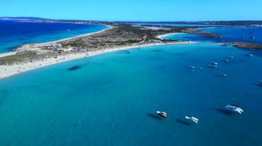 Platja de ses Illetes 'in açık turkuaz okyanuslu plaj formenterasını ve açık bir gökyüzü altında dinlenen insanları gösteren hava manzarası. statik üç ayaklı insansız hava aracı 