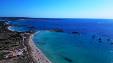 Platja de ses Illetes 'in açık turkuaz okyanuslu plaj formenterasını ve açık bir gökyüzü altında dinlenen insanları gösteren hava manzarası. geniş yörünge görünümü dronu 