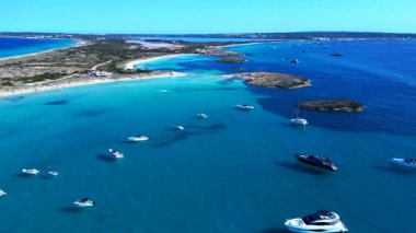 Balear Adaları 'ndaki kumlu bir sahil şeridi yakınlarında kristal berrak sularda yüzen sayısız lüks yat ve tekne. panorama genel bakış statik üç ayaklı insansız hava aracı 