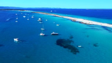 Balear Adaları 'ndaki kumlu bir sahil şeridi yakınlarında kristal berrak sularda yüzen sayısız lüks yat ve tekne. panorama genel bakış statik üç ayaklı insansız hava aracı 