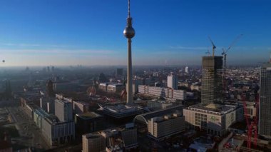 Berlins ikonik Fernsehturm 'un berrak mavi gökyüzünün altındaki şehir manzarasına hakim olduğunu gösteren hava manzarası. Panorama genel görünümlü İHA 'yı eğ