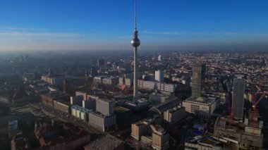 Berlins ikonik Fernsehturm 'un berrak mavi gökyüzünün altındaki şehir manzarasına hakim olduğunu gösteren hava manzarası. durağan tripod havada süzülen panorama drone