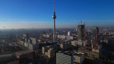 Berlins ikonik Fernsehturm 'un berrak mavi gökyüzünün altındaki şehir manzarasına hakim olduğunu gösteren hava manzarası. durağan tripod havada süzülen panorama drone