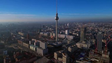 Berlins ikonik Fernsehturm 'un berrak mavi gökyüzünün altındaki şehir manzarasına hakim olduğunu gösteren hava manzarası. panorama yörünge dronu