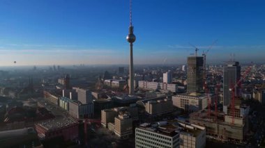 Berlins ikonik Fernsehturm 'un berrak mavi gökyüzünün altındaki şehir manzarasına hakim olduğunu gösteren hava manzarası. Sinek ileri itme panorama genel görünüm drone