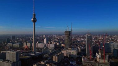 Berlins ikonik Fernsehturm 'un berrak mavi gökyüzünün altındaki şehir manzarasına hakim olduğunu gösteren hava manzarası. panorama genel bakış dönüş panosu sol drone 'a