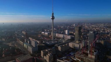 Berlins ikonik Fernsehturm 'un berrak mavi gökyüzünün altındaki şehir manzarasına hakim olduğunu gösteren hava manzarası. İHA panorama genel görüntüsü alçalıyor