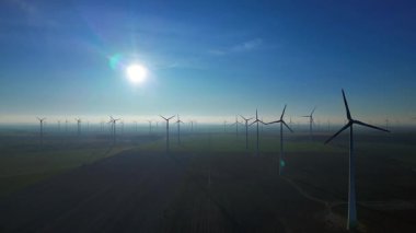 Uçsuz bucaksız bir alanda dönen rüzgar türbinleri açık mavi gökyüzü altında sürdürülebilir güç üreterek ekolojik ilerlemeyi teşvik ediyor. panorama genel bakış statik üç ayaklı insansız hava aracı