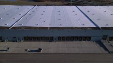 Verimli lojistik ve kargo işlemleri için sayısız yükleme rıhtımı bulunan geniş bir dağıtım merkezi binasının havadan görüntüsü. Yukarıdan aşağıya doğru uçur