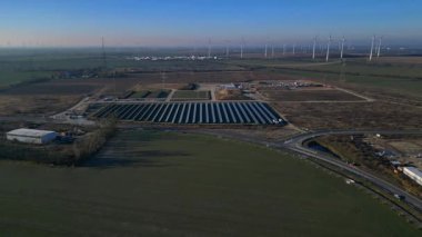 Bir güneş çiftliği ve rüzgar parkının hava görüntüsü, açık bir günde kırsal alanda sürdürülebilir enerji kaynaklarını birleştiriyor. Geniş yörünge genel bakış drone hız rampası hiper hareket zaman aşımı