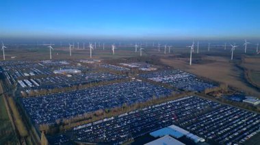 Depoları ve tren rayları olan, rüzgar türbinleriyle çevrili büyük bir dağıtım merkezinde yeni arabalar bekliyor. Yukarıdan drone atışı