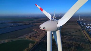 Rüzgâr türbininin kapatılması birçok türbin, güneş panelleri ve arka planda açık mavi gökyüzünün altında bir otopark ile yakın çekim. panorama yörünge dronu