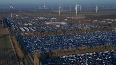 Depoları ve tren rayları olan, rüzgar türbinleriyle çevrili büyük bir dağıtım merkezinde yeni arabalar bekliyor. panorama genel görüntüleme İHA 'sı yukarıdan aşağıya