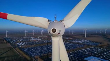 Rüzgâr türbininin kapatılması birçok türbin, güneş panelleri ve arka planda açık mavi gökyüzünün altında bir otopark ile yakın çekim. Ters İHA uçuşu