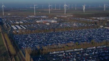 Depoları ve tren rayları olan, rüzgar türbinleriyle çevrili büyük bir dağıtım merkezinde yeni arabalar bekliyor. rotasyon pan 'dan sağ drona