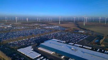 Depoları ve tren rayları olan, rüzgar türbinleriyle çevrili büyük bir dağıtım merkezinde yeni arabalar bekliyor. panorama genel görünüm dönüş panosu sağ drone 'a