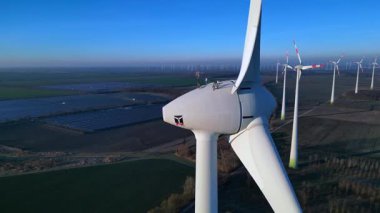 Rüzgâr türbininin kapatılması birçok türbin, güneş panelleri ve arka planda açık mavi gökyüzünün altında bir otopark ile yakın çekim. Yukarıdan drone atışı