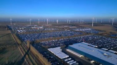 Depoları ve tren rayları olan, rüzgar türbinleriyle çevrili büyük bir dağıtım merkezinde yeni arabalar bekliyor. Ters İHA uçuşu