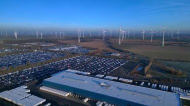 Depoları ve tren rayları olan, rüzgar türbinleriyle çevrili büyük bir dağıtım merkezinde yeni arabalar bekliyor. rotasyon tavası sol drona