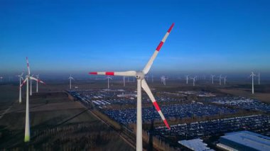 Rüzgar türbinleri dönüyor, büyük bir rüzgar çiftliği, sanayi tesisleri ve aşağıdaki otoparkta temiz yenilenebilir enerji üretiyor. panorama yörünge dronu