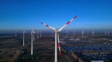 Rüzgar türbinleri dönüyor, büyük bir rüzgar çiftliği, sanayi tesisleri ve aşağıdaki otoparkta temiz yenilenebilir enerji üretiyor. Ters panorama görünümü dronu uçur