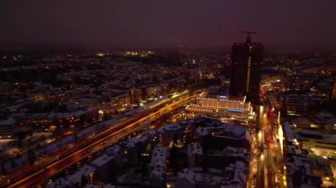 Kış alacakaranlığında şehir manzarası, taze karla kaplı binalar ve sokaklar sıcak ışıklarla soğuk bir şehir manzarası yaratıyor. Yukarıdan insansız hava aracı görüntüsü
