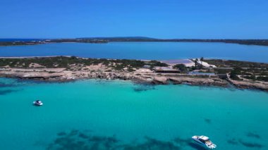 Temiz turkuaz suyu, kayalık kıyısı, sahil barı ve Es Estany tuz düzlüklerinin sulak alanları olan kıyı şeridi. panorama genel görünümü dolly sol drone